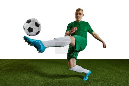 Foto de Hombre competitivo, futbolista en uniforme verde entrenando, pateando pelota con pierna contra fondo blanco. Concepto de deporte profesional, acción, estilo de vida, competencia, hobby, entrenamiento, anuncio - Imagen libre de derechos