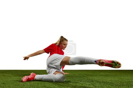 Foto de Atleta femenina motivada, chica joven, jugador de fútbol pateando la pelota en movimiento en la hierba del campo contra el fondo blanco. Concepto de deporte profesional, acción, estilo de vida, competencia, hobby, entrenamiento, anuncio - Imagen libre de derechos