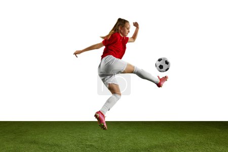 Foto de Imagen dinámica de atleta femenina, joven, futbolista en movimiento con pelota en el campo de deportes sobre fondo blanco. Concepto de deporte profesional, acción, estilo de vida, competencia, entrenamiento, anuncio - Imagen libre de derechos