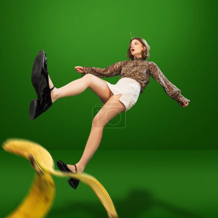 Téléchargez les photos : Image créative avec jeune fille en chemisier élégant imprimé animal et short blanc glissant sur la peau de banane et tombant. Concept d'émotions, style de vie, plaisir, shopping, mode, publicité - en image libre de droit