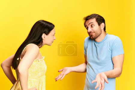 Photo for Young woman emotionally talkin to man, asking questions against yellow studio background. Man making excuses. Concept of friendship, relationship, communication, emotions, lifestyle, ad - Royalty Free Image