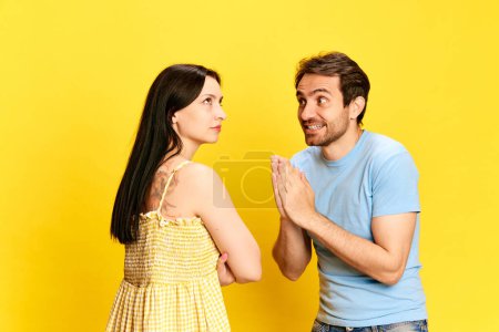 Photo for Man emotionally talking to offended woman and asking for forgiveness against yellow studio background. Concept of friendship, relationship, communication, emotions, lifestyle, ad - Royalty Free Image