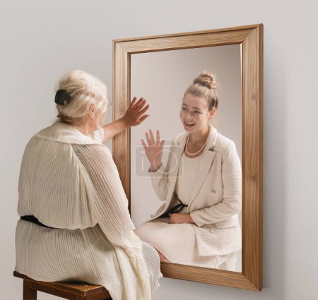 Téléchargez les photos : Collage conceptuel créatif. Image tendre d'une femme âgée regardant dans un miroir et souriant à son jeune reflet de soi. Retour au passé. Concept de présent, passé et futur, âge, mode de vie, souvenirs, publicité - en image libre de droit