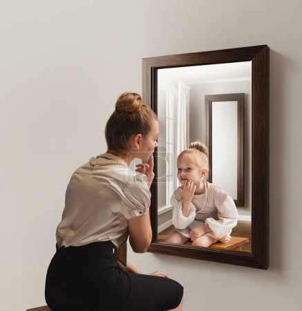 Photo for Creative conceptual collage. Young woman looking in mirror and seeing her little self. Back to childhood memories. Concept of present, past and future, age, lifestyle, emotions, generation, ad - Royalty Free Image