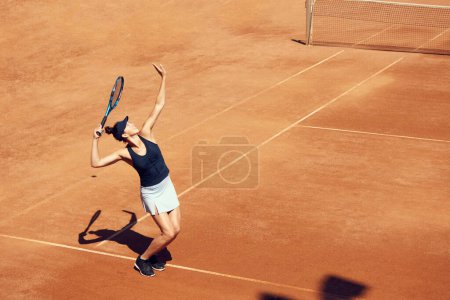 Téléchargez les photos : Image du joueur de tennis professionnel en mouvement, jeune femme servant le ballon avec raquette, entraînement au stade en plein air, court. Concept de sport, passe-temps, mode de vie actif, santé, force, publicité - en image libre de droit