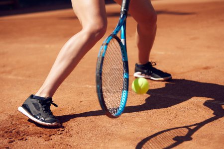 Photo for Cropped image of female legs in sportswear and tennis racket with ball over floor background with shadows. Open air tennis court. Concept of sport, hobby, active lifestyle, health, strength, ad - Royalty Free Image