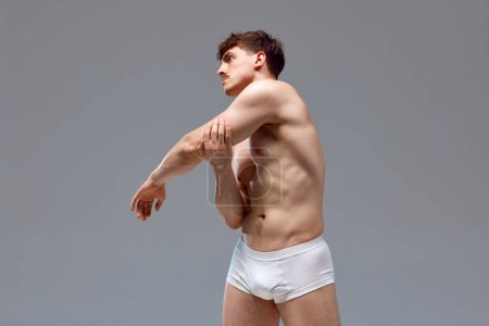 Photo for Back pains. Young man with relief, muscular, strong body, back posing shirtless in underwear against grey studio background. Concept of mans beauty, sport, health, athletic body, medicine - Royalty Free Image