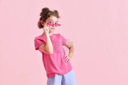 Photo for Portrait of beautiful little girl child in casual clothes, sunglasses posing against pink studio background. Concept of emotions, childhood, education, fashion, lifestyle, ad - Royalty Free Image