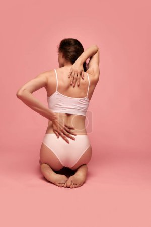 Photo for Back pains. Rear view image of female body, shoulders, back against pink studio background. Model posing in underwear. Concept of female beauty, body care, fitness, sport, health, figure, ad - Royalty Free Image