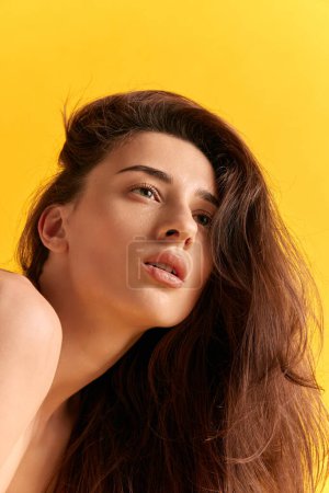 Photo for Portrait of young beautiful woman wit brown wavy hair posing against yellow studio background. Self-care. Cosmetology. Concept of female beauty, skin care, cosmetics, spa, health, figure, ad - Royalty Free Image