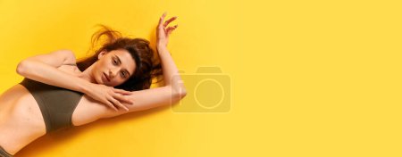 Foto de Retrato de una joven hermosa mujer tierna tumbada en el suelo, posando en ropa interior sobre fondo amarillo del estudio. Concepto de belleza femenina, cuidado corporal, cosmetología, spa, fitness, salud, figura, anuncio. Banner - Imagen libre de derechos