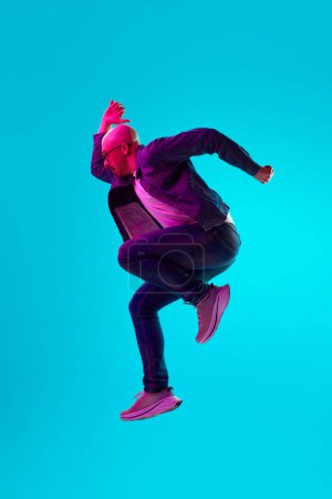 Photo for Portrait of young bald man with moustache in stylish casual clothes jumping against blue studio background in neon light. Concept of human emotions, facial expression, lifestyle - Royalty Free Image