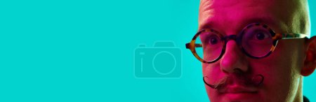 Photo for Close-up cropped image of male face, young bald man with moustache in glasses against blue studio background in neon light. Concept of human emotions, facial expression, lifestyle - Royalty Free Image