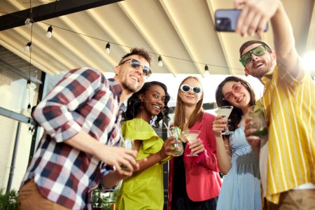 Photo for Group of young people, friends taking selfie together, meeting at cafe, drinking cocktails, talking, celebrating. Joyful time. Concept of friendship, meeting, party, communication, alcohol drinks - Royalty Free Image