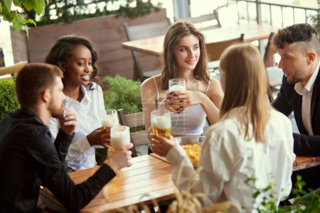 Photo for Young business people, colleagues meeting together at cafe, bar after work to drink beer, talk and spend relaxing time. Concept of leisure time, business, communication, fun, alcohol drink - Royalty Free Image