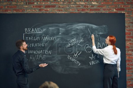 Photo for Man and woman, colleagues writing on blackboard marketing strategies of brand development. Building successful business strategies. Concept of business, planning, strategy, brainstorming, analytics - Royalty Free Image