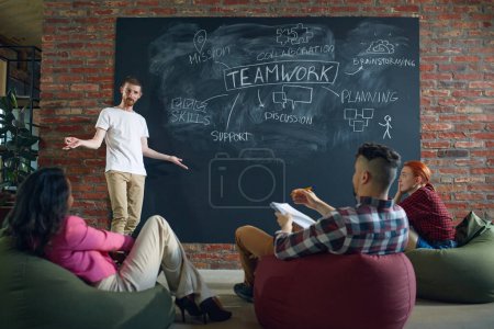 Photo for Workshop for employees. Young people, colleagues sitting in class, talking and discussing about teamwork strategies. Successful cooperation. Concept of business, planning, brainstorming, analytics, ad - Royalty Free Image