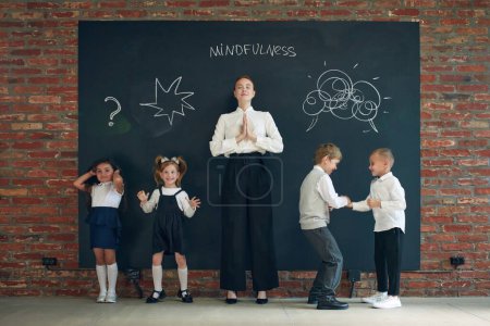 Photo for Mindfulness. Young woman in formal wear standing by blackboard with little children. Education, business and psychology lessons. Concept of business, education, lessons, games, study, psychology, ad - Royalty Free Image