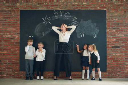 Photo for Young emotive woman standing by blackboard with drawn cons, playing and teaching kinds. Brainstorming, education. Concept of business, education, lessons, games, study, psychology, ad - Royalty Free Image