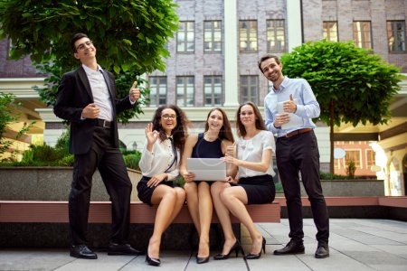 Photo for Group of employees, business people, project leaders sitting on bench outside office on daytime and working online on laptop. Business, career development, ambitions, success, office lifestyle concept - Royalty Free Image