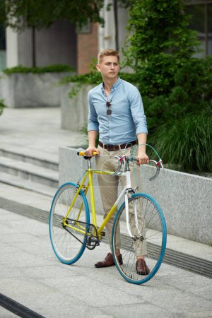 Photo for Young handsome businessman, office worker in stylish smart casual clothes standing outdoors with bike. Beautiful urban background. Concept of business, active lifestyle, fashion, youth, ecology - Royalty Free Image