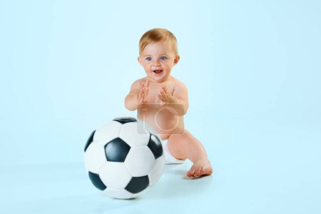Photo for Happy, smiling little baby, toddler in diaper playing with football ball against light blue studio background. Concept of childhood, newborn lifestyle, happiness, care. Copy space for ad - Royalty Free Image