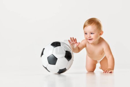 Photo for Happy, smiling little baby, toddler in diaper crawling and playing with football ball against white studio background. Concept of childhood, newborn lifestyle, happiness, care. Copy space for ad - Royalty Free Image