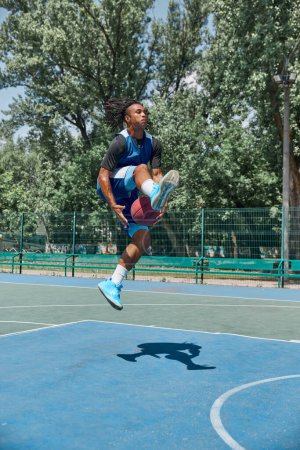 Photo for Slam dunk. Full-length image of young man in motion, playing basketball outdoors on sportsground on warm day. Concept of professional sport, competition, hobby, game, active lifestyle - Royalty Free Image