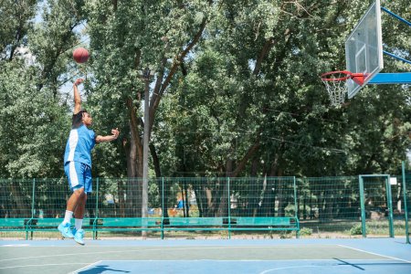 Photo for Young sportive man, athlete in blue unifroman training, playing basketball outdoors on sportsground on warm sunny day. Concept of professional sport, competition, hobby, game, active lifestyle - Royalty Free Image