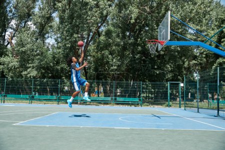 Photo for Young sportive man, athlete in blue unifroman training, playing basketball outdoors on sportsground on warm sunny day. Concept of professional sport, competition, hobby, game, active lifestyle - Royalty Free Image