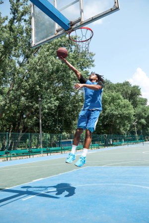 Photo for Concentrated young man, athlete in blue uniform playing basketball, throwing ball into basket. Outdoors training. Concept of professional sport, competition, hobby, game, active lifestyle - Royalty Free Image