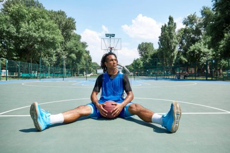 Photo for Young guy in blue uniform, basketball player sitting and resting after game. Outdoor sportsground. Concept of professional sport, competition, hobby, game, active lifestyle - Royalty Free Image