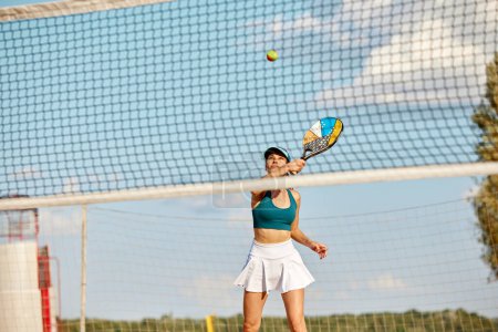 Photo for Dynamic image of young woman playing beach tennis, hitting ball with racket. Outdoor training on warm summer day. Concept of sport, leisure time, active lifestyle, hobby, game, summertime, ad - Royalty Free Image