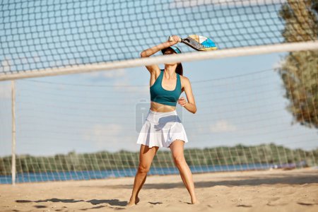 Téléchargez les photos : Jeune femme jouant au paddle tennis, frappant balle avec raquette. Entraînement en plein air sur la plage par une chaude journée d'été. Concept de sport, temps libre, mode de vie actif, passe-temps, jeu, été, annonce - en image libre de droit