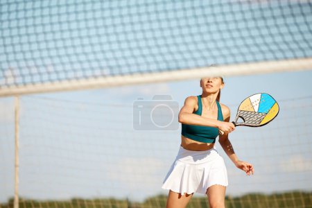 Téléchargez les photos : Jeune femme sportive jouant à la plage, au paddle tennis, frappant balle avec raquette. Entraînement en plein air par une chaude journée d'été. Concept de sport, temps libre, mode de vie actif, passe-temps, jeu, été, annonce - en image libre de droit