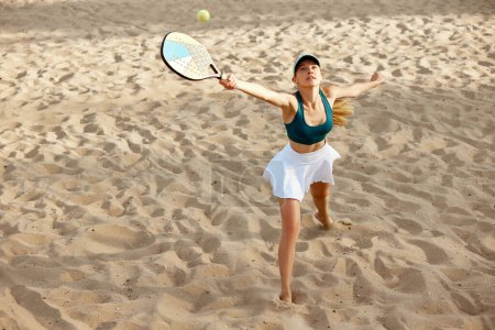Foto de Imagen de vista superior de una mujer joven jugando al pádel, tenis de playa, golpeando la pelota con raqueta en movimiento. Competencia. Concepto de deporte, tiempo libre, estilo de vida activo, hobby, juego, verano, anuncio - Imagen libre de derechos