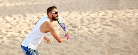 Téléchargez les photos : Image dynamique du jeune homme jouant au tennis de plage, frappant balle avec raquette. Entraînement en plein air par une chaude journée d'été. Vue de dessus. Concept de sport, temps libre, mode de vie actif, passe-temps, jeu, été, annonce - en image libre de droit