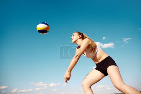 Téléchargez les photos : Jeunes femmes athlétiques jouant au beach-volley lors d'une chaude journée d'été en plein air. Frapper la balle avec les mains. Concentration. Concept de sport, mode de vie actif et sain, passe-temps, été, publicité - en image libre de droit