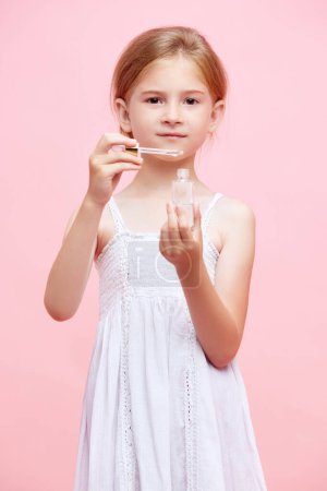 Photo for Little girl, child applying face serum, taking care after skin against pink studio background. Concept of skincare, childhood, kids cosmetology and health, beauty, organic products, ad - Royalty Free Image