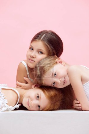 Téléchargez les photos : Portrait de petits beaux enfants, filles posant ensemble sur fond de studio rose. Bien-être. Concept de soins de la peau, enfance, cosmétologie et santé, beauté, produits biologiques, publicité - en image libre de droit