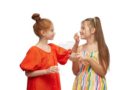Photo for Little girls, children taking care after skin, applying face cream against white studio background. Concept of skincare, childhood, cosmetology and health, beauty, organic products, ad - Royalty Free Image