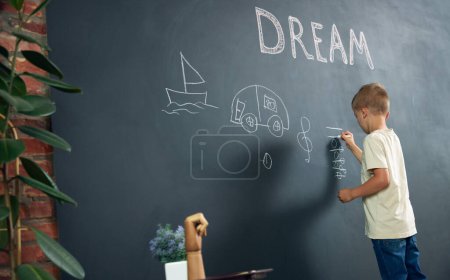 Foto de Niño, niño de pie en negro y dibujando sus sueños sobre ser músico. Imaginación. Psicología y pensamiento creativo. Concepto de escuela, educación, infancia, conocimiento, estilo de vida - Imagen libre de derechos