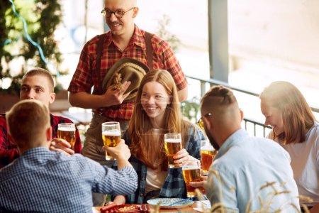 Photo for Group of cheerful young people, friends meeting at cafe, pub, spending time together, drinking beer. Celebration and fun. Concept pktoberfest, traditional taste, friendship, leisure time, enjoyment - Royalty Free Image