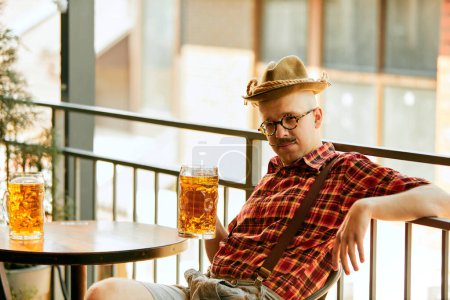 Photo for Yopougon stylish man with moustache, in checkered shirt and fedora hat sitting at pub and drinking lager beer. Concept of oktoberfest, traditional taste, friendship, leisure time, enjoyment - Royalty Free Image