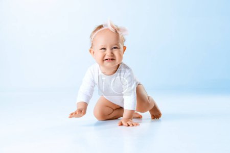 Photo for Cute, lovely, funny baby girl, child, toddler smiling and crawling on floor against blue studio background. Concept of childhood, family, newborn lifestyle, happiness, care. Copy space for ad - Royalty Free Image