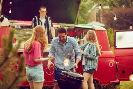 Photo for Group of young people, friends spending time outdoors, having barbecue party, cooking, drinking cocktails, talking. Countryside meeting. Concept of friendship, leisure time, weekends, summer, party - Royalty Free Image