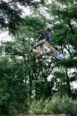 Téléchargez les photos : Activité estivale. Jeune homme sportif à vélo bmx en forêt, faire des tours dangereux et difficiles, sauter à vélo. Concept de mode de vie actif, sport, extrême, dynamique, passe-temps, freestyle - en image libre de droit