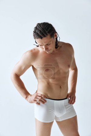 Photo for Muscular, strong, athletic man with braids posing shirtless in white underwear, boxers against grey studio background. Concept of mens beauty, body care, sport, wellness, healthy lifestyle, ad - Royalty Free Image