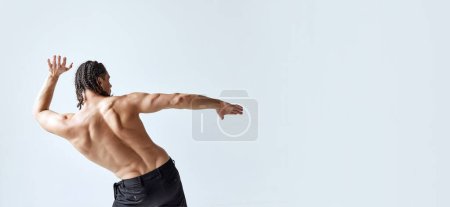 Foto de Hombre atlético y musculoso posando sin camisa en pantalones sobre fondo gris estudio. Espalda fuerte y saludable. Concepto de belleza para hombre, cuidado corporal, moda, bienestar, estilo de vida saludable, anuncio. Banner - Imagen libre de derechos