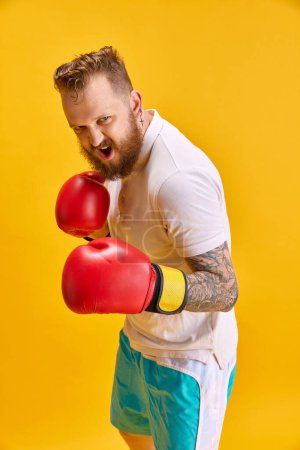 Photo for Bearded emotional man in sportswear and boxing gloves against bright yellow background. Ambitious sportsman. Concept of sport, strength, fashion, meme emotions, lifestyle, ad - Royalty Free Image